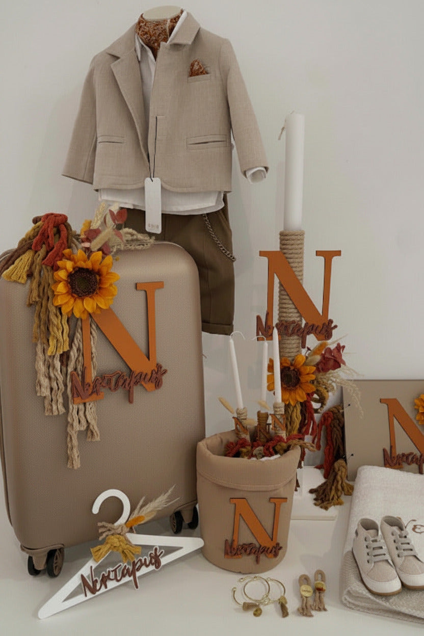 A styled autumn-themed outfit display featuring a beige boys' blazer over a white shirt and brown shorts on a mannequin, alongside matching beige luggage, a fabric pot, a hanger, and accessories decorated with sunflowers, tassels, and wooden letters.